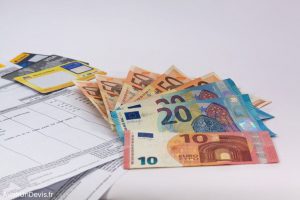 Des billets de 10, 20, 50 euros posés à côté d'une facture