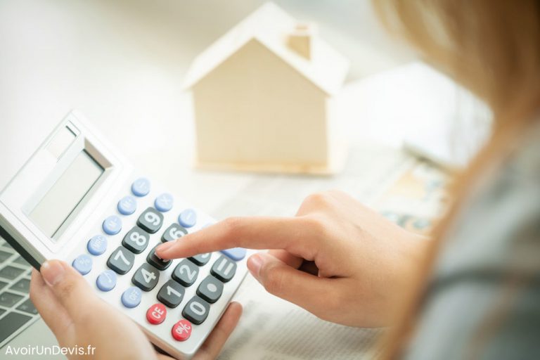 Une femme fait un calcul avec une calculatrice devant une maison miniature