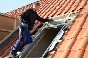 Un couvreur installe des fenêtres de toit "Velux" sur un toit en tuiles rouges.